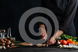 Professional chef cuts with knife chicken fillet for preparing meat filling for pie. Ingredients for cooking on the background.