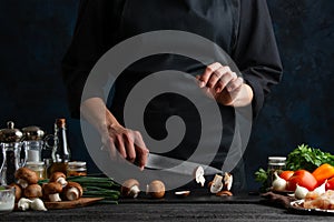 Professional chef cuts with knife mushrooms for preparing meat filling for pie. Ingredients for cooking on the background. Dark