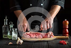 Professional chef cuts meat with a knife before baking. Spices on kitchen table in a restaurant for preparing a delicious lunch