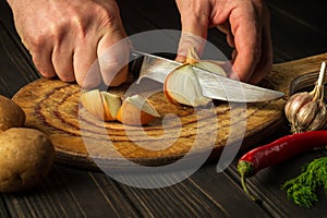 Professional chef cuts the onion with a knife on a cutting board for making soup for lunch. Vegetable diet idea. Work environment