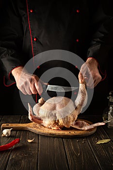A professional chef cuts raw chicken with a knife in the kitchen. Cooking chicken for lunch. European cuisine