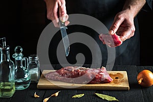 Professional chef cutting beef meat with knife on kitchen, cooking food. Vegetables and spices on the kitchen table to prepare