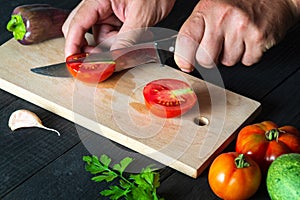 Professional chef is cutting a red tomato in a restaurant kitchen, a for a salad. Close-up of the hands of the cook during work on