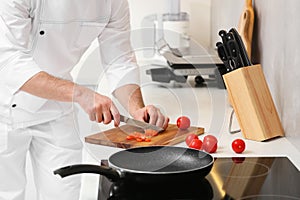 Professional chef cutting tomatoes in kitchen, closeup