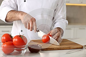 Professional chef cutting tomatoes at white marble table indoors, closeup