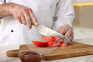 Professional chef cutting tomatoes at white marble table indoors, closeup