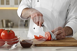 Professional chef cutting tomatoes at white marble table indoors, closeup