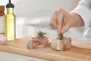 Professional chef decorating delicious meat with thyme at white table, closeup