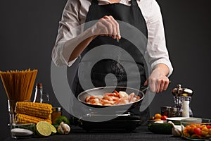 Professional chef fries and salts the shrimp on a background of vegetables. Seafood and wholesome food photo