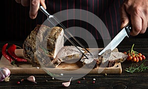 Professional chef holding a knife and fork cuts a beef steak on a kitchen cutting board. Delicious lunch with baked meat with