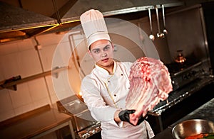 Professional chef holding raw bbq beef ribs on the background of vegetables. Chief chef preparing meat for grilling in the kitchen