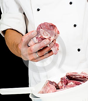 A professional chef in jacket, holding a lump of meat