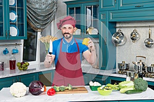 Professional Chef on kitchen cooking vegetables. Cook in red apron and cap. Man holds knife and paprika in hands on kitchen.