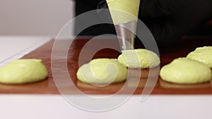 professional chef making base for preparation macaron dessert. Close-up of extruding light green creme from piping bag
