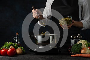 The professional chef pours canned peas in the pot with boiling water on dark blue background. Backstage of preparing meal with