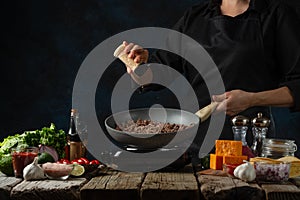 Professional chef pours dry mustard into frying meat in pan for cooking filling for tacos. Backstage of preparing traditional