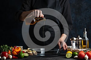 Professional chef pours oil into glass bowl for cooking baked potato with seafood. Backstage of preparing delicious dinner on dark