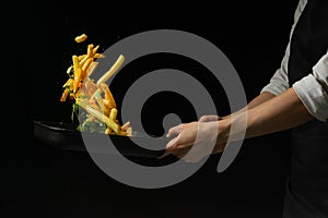 Professional chef prepares french fries with greens. Cooking tasty but harmful food on a dark background. Horizontal view photo