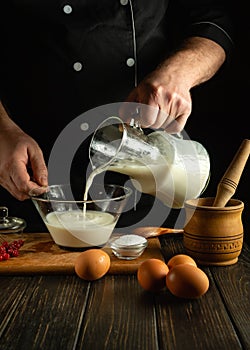 A professional chef prepares a milkshake with fruits in the kitchen using a hand-held electric mixer. The cook pours milk into a