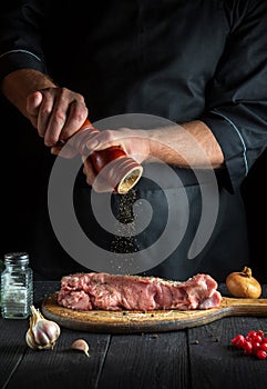 Professional chef prepares raw veal meat. Before baking, the chef adds pepper to beef. National dish is being prepared in the