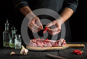The professional chef prepares raw veal meat. Before baking cook puts the viburnum on the beef. National dish is being prepared in