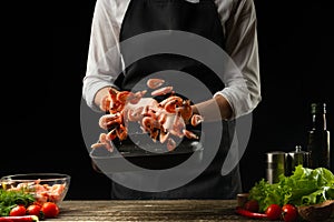 Professional chef prepares a salad of fresh shrimp, and vegetables on a dark background, freezing in motion. Seafood and healthy