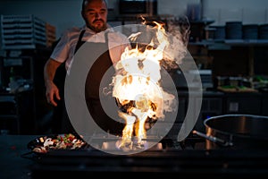 Professional chef preparing meal, flambing indoors in restaurant kitchen.