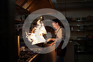 Professional chef preparing meal, flambing indoors in restaurant kitchen.