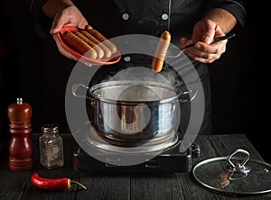 Professional chef puts Vienna sausage in a saucepan. Working environment in the kitchen of a restaurant or cafe. Preparing