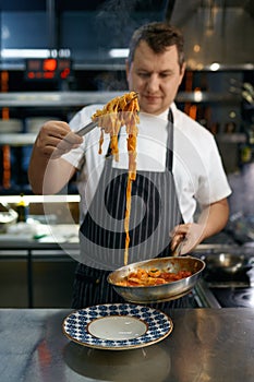 Professional chef serving freshly cooked pasta on plate
