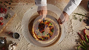 Professional chef slicing pizza by round cutter knife in restaurant kitchen.