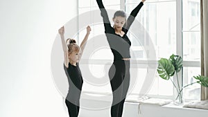 Professional cherleading trainer dancing with little girl, moving synchronically at dance class