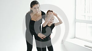Professional cherleading trainer dancing with little girl, moving synchronically at dance class
