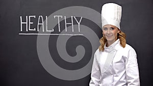 Professional chief cook smiling against blackboard with health word, nutrition