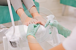 Professional chiropodist holding spray while making pedicure