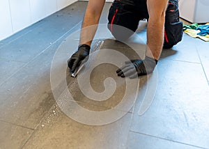 Professional cleaner cleaning grout with a brush blade and foamy soap on a gray tiled bathroom floor photo