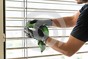 Professional cleaner deep cleaning window blinds in an apartment with a green microfiber cloth