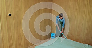 Professional cleaner in uniform washing floor in the hotel room or apartment bedroom. Cleaning service concept.