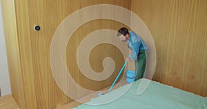 Professional cleaner in uniform washing floor in the hotel room or apartment bedroom. Cleaning service concept.