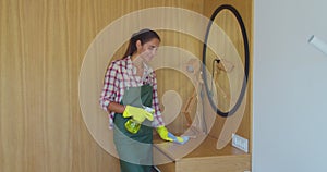 Professional cleaner in uniform wiping dust from the furniture in the hotel room or apartment bedroom. Cleaning service
