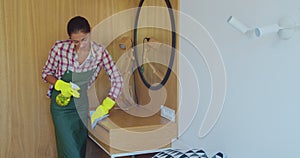 Professional cleaner in uniform wiping dust from the furniture in the hotel room or apartment bedroom. Cleaning service