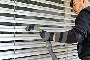 Professional cleaner vacuum cleaning window blinds on an apartment balcony