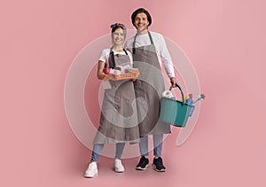 Professional Cleaners. Happy Couple In Aprons With Cleaning Tools In Hands