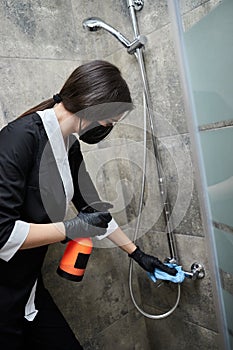 Professional Cleaning service company employee in rubber gloves with spray bottle and blue rag cleaning a shower in bathroom
