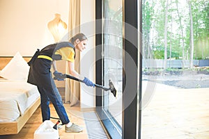 Professional cleaning service. woman in uniform and gloves sponge washes panoramic windows in the cottage. washing steam