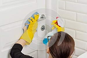 Professional cleaning services. Woman worker in rubber gloves doing cleaning in the bathroom, cleaning door with rag and detergent