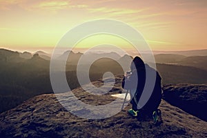 Professional on cliff. Nature photographer takes photos with mirror camera on peak of rock.