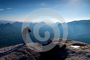 Professional on cliff. Nature photographer takes photos with mirror camera on peak of rock. Dreamy blue fogy landscape,