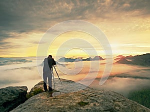 Professional on cliff. Nature photographer takes photos with mirror camera on peak of rock. Dreamy fog