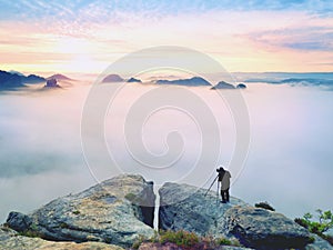 Professional on cliff. Nature photographer takes photos with mirror camera on peak of rock. Dreamy fog